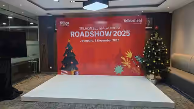 Panggung Telkomsel Roadshow 2025 dengan backdrop merah, layar display, dan dekorasi pohon Natal.
