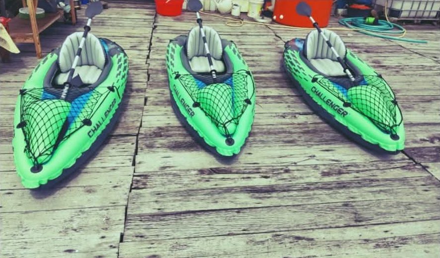 Tiga perahu kano / kayak tiup hijau di atas dermaga kayu Injros View