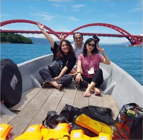 Tamu di atas perahu di Teluk Youtefa dengan Jembatan Merah (Jembatan Youtefa) di latar belakang